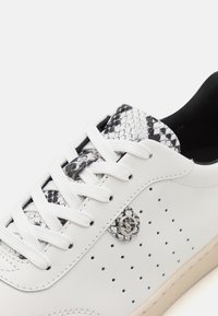 Sneaker in pelle bianca con accenti a motivo pitone in bianco e nero, perforazioni sui lati, lacci bianchi piatti e suola beige.