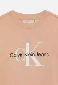 Sweatshirt rose clair avec un col rond, comportant un « K » blanc bien en vue et le texte noir « Calvin Klein Jeans » sur le devant.