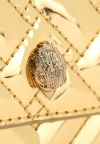 Złota pikowana torebka z połyskującym wykończeniem ze skóry, charakterystycznym ukośnym przeszyciem i ozdobnym srebrnym zapięciem w kształcie liścia.