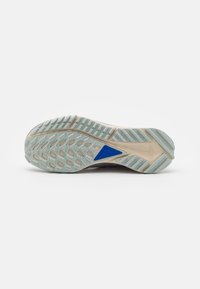 Semelle de chaussure de sport beige clair avec une prise en caoutchouc texturée, présentant un accent bleu. Comprend un mélange de motifs géométriques pour la traction.