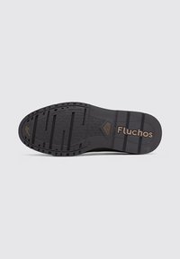 Suela de zapato de goma negra con patrones texturizados, múltiples surcos para tracción y un logotipo marrón "Fluchos" estampado en el lateral.