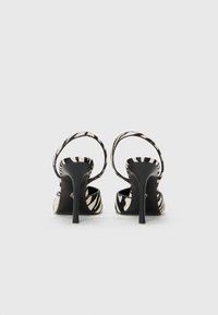 Black and white zebra print high-heeled sandals with a smooth texture, open back, and thin ankle straps. Stiletto heel design.
