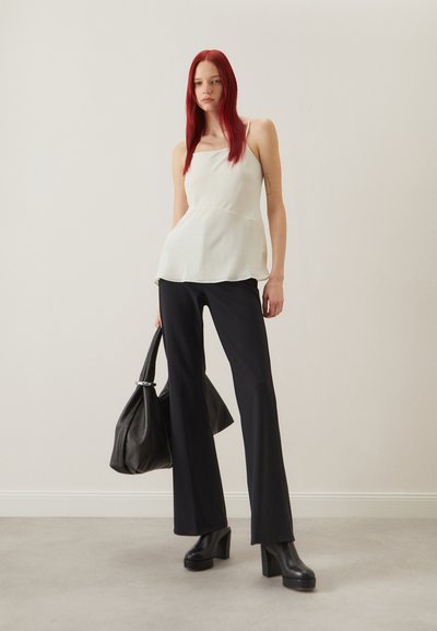 Top peplum blanc avec des fines bretelles, associé à un pantalon noir long et des bottes plates-formes noires épaisses. Le modèle tient un sac à main noir.