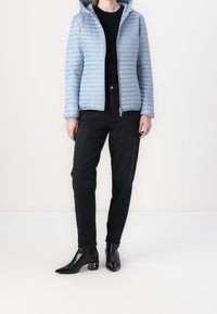 Lyseblå puffjakke med hætte, med et quiltet mønster, kombineret med sorte højtaljede bukser og spidse sorte hælede støvler.