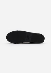 Suela de zapato de goma negra con superficie texturizada, presenta un logo impreso y patrón estriado para tracción. Forma redondeada, diseño minimalista.