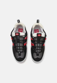 Zapatillas deportivas negras con paneles de malla, acentos rojos y plantillas blancas. Presentan cordones negros y un collar acolchado para mayor comodidad.