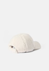Casquette de couleur crème en matériau doux et duveteux ; présente une couronne arrondie et un bord incurvé avec des détails de couture visibles.