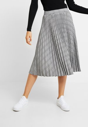 Zwart-witte geruite geplooide rok met een aansluitende tailleband, gecombineerd met witte sneakers. Heeft een gelaagde textuur en een midi-lengte ontwerp.