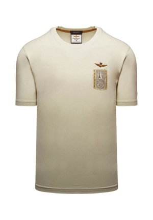 T-shirt beige a maniche corte con collo rotondo, con una piccola toppa e un emblem con ali ricamato sul petto sinistro.