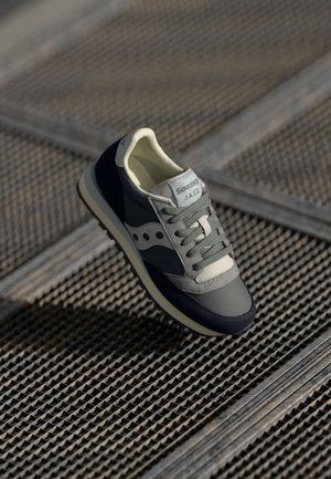 Saucony Jazz sneaker in grey, navy, and light green. Features mesh and suede materials, round laces, padded collar, and branded tag.