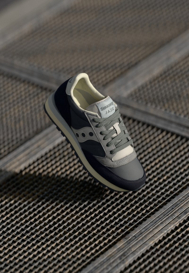 Sneaker Saucony Jazz in grigio, blu navy e verde chiaro. Caratterizzato da materiali in rete e suede, lacci rotondi, colletto imbottito e etichetta con marchio.