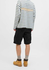 Pasiasta koszula z długim rękawem w kolorze kremowym i niebieskim, czarne szorty cargo oraz beżowe buty. Zauważalne detale to tekst "ORIGINALS" na koszuli.