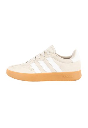 Beige lage Adidas sneaker met witte strepen en een rubberen zool, zijaanzicht.