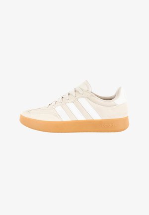 Beige lage Adidas sneaker met witte strepen en een rubberen zool, zijaanzicht.