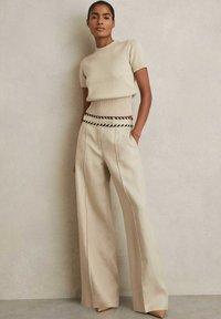 Top corto a maniche corte in maglia beige con una trama a coste; abbinato a pantaloni a gamba larga a vita alta con una cintura a motivo bianco e nero.