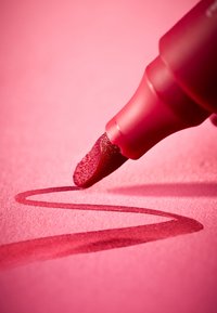 Pennarello con punta in feltro, di colore rosso intenso, che traccia una linea liscia su carta rosa, mostrando la trama e un leggero dettaglio di ombra.