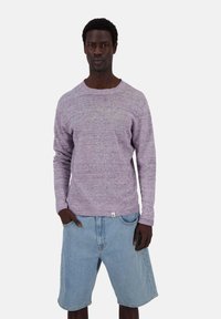 Hellvioletter, gestrickter Pullover mit einem strukturierten Muster, Rundhalsausschnitt und gerippten Bündchen, kombiniert mit hellblauen Jeansshorts.