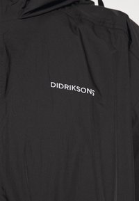 Chaqueta impermeable negra con una textura suave, que cuenta con una capucha y el nombre de la marca "DIDRIKSONS" bordado en blanco en la parte posterior.