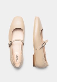 Ballerines Mary Jane en cuir beige avec un bout rond, une bride à la cheville et un faible talon en bois. Texture lisse et détails de couture minimalistes.