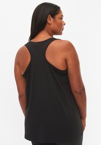 Musta urheilullinen tank top, jossa on urheilurintakehys, sileä pinta ja rento istuvuus. Pituus ulottuu hieman lantion alapuolelle.