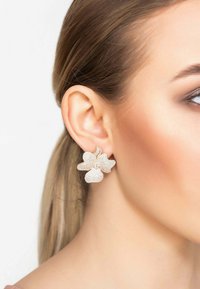 Gold flower-shaped earrings with a textured surface and small clear gems. Visible fine details on petals enhance the design.