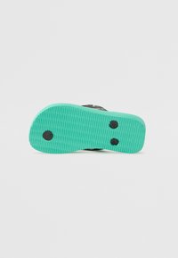 Green rubber sole with textured grooves and black circular accents. Upper part features a layered black material design.