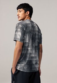 Graues Kurzarm-T-Shirt mit einem geometrischen Muster in verschiedenen Schattierungen, weicher Textur und lockerer Passform, von hinten gezeigt.