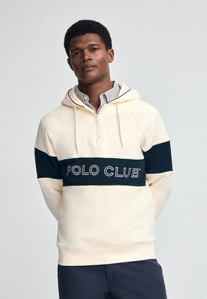 Cremefarbener Hoodie mit dunkelblauem horizontalem Streifen, auf dem "POLO CLUB" in weißen Buchstaben steht. Er hat einen Reißverschluss am Hals und gerippte Bündchen.