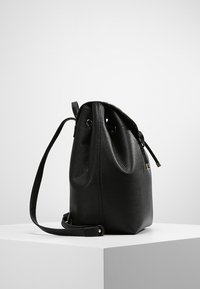 Bolso tipo bucket de piel negra con un acabado texturizado, cierre de cordón y correa ajustable. Presenta un pequeño acento en tono dorado.