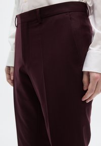 Μπορντό παντελόνι με ραφή, με λείο ύφασμα, διαθέτει πλαϊνές τσέ πες και ίσια εμπρός όψη, συνδυασμένο με ένα κρεμ πουκάμισο με κουμπιά.