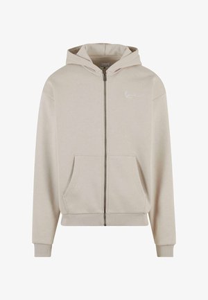 Beež kapuutsiga dressipluus, millel on eesmine tasku, soonikkoes mansetid ja alläär ning väike valge logo rinnal. Valmistatud pehmest, tekstureeritud kangast.