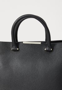 Sac fourre-tout en cuir noir avec une surface texturée, doté de deux poignées solides et d'un petit accent métallique sur le haut à l'avant.