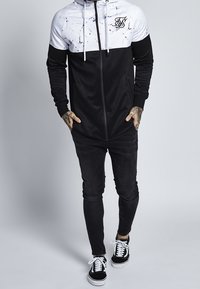 Svart och vit zip-hoodie med ett marmor mönster på den övre delen, kombinerad med svarta slim-fit byxor och svarta sneakers.
