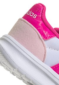 Zapatilla con una base texturizada blanca, acentos en rosa y panel lateral brillante rosa. Logo de Adidas mostrado de manera destacada en blanco.