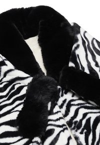 Palton din blană artificială cu imprimeu de zebra, având dungi negre și albe, o textură pufoasă și un guler lat cu accente negre moi.