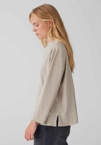 Hellgraues, geripptes Langarmoberteil mit hohem Kragen und seitlichen Schlitzen, das eine lockere Passform und eine weiche Textur aufweist.