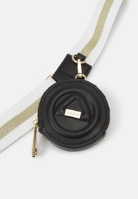 Porte-monnaie rond en cuir noir avec un motif géométrique en relief, des accessoires en métal doré et une bandoulière blanche amovible avec une bande dorée.
