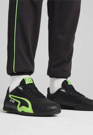 Baskets de sport noires avec des accents verts, dotées d'une surface texturée, d'un système de laçage et d'un design ergonomique pour une flexibilité et un confort optimaux.