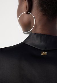 Black satin shirt collar with a gold "M" hardware accent. Large silver hoop earring visible, showcasing smooth, shiny texture.