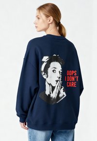 Felpa blu navy con grafica di una donna con un ritratto corto in bianco e nero. Il testo recita "OOPS NON MI IMPORTA" in rosso.