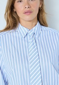 Hellblau-weiß gestreiftes Hemd mit spitzem Kragen und einer Krawatte im gleichen Muster, gefertigt aus glattem Stoff mit weicher Textur.