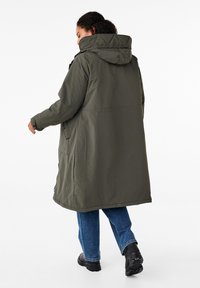 Maslinasto zelena, duga parka jakna s kapuljačom, s bočnim džepovima i ležernim krojem. Tkanina je glatka i otporna na vodu.