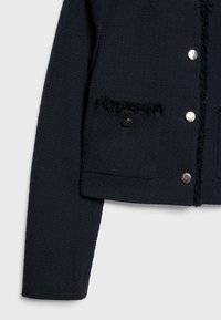 Veste texturée bleu marine avec un design court, deux poches avant aux bords effilochés et des boutons-pression métalliques.