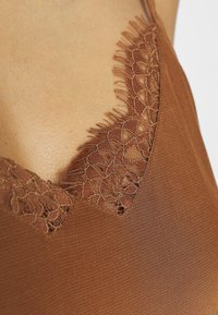 Top in raso marrone con un bordo in pizzo testurizzato all'escollature, effetto ondulato e spalline sottili. Tessuto liscio.
