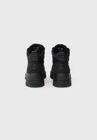 Černé středně vysoké boty s texturovaným textilním svrškem, kulatými logovými akcenty, polstrovaným límcem a silnou gumovou podrážkou s označením značky.