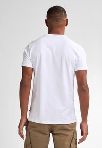 Bílý krátký rukáv tričko, bavlněný materiál, kulatý výstřih, jednoduchý design, nošeno s khaki cargo šortkami, bez viditelných log a vzorů.