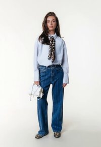 Μπλε ριγέ πουκάμισο με φαρδιά εφαρμογή, συνδυασμένο με ψηλόμεσα μπλε τζιν με λεπτές ρίγες. Διαθέτει φουλάρι με λεοπάρ μοτίβο και λευκή τσάντα χειρός.