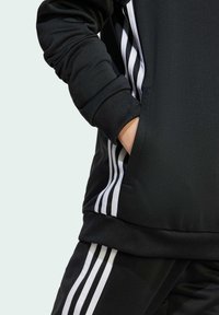 Felpa sportiva nera con strisce bianche lungo i lati. Presenta polsini a coste e una tasca sulla parte anteriore. Tessuto liscio e strutturato.