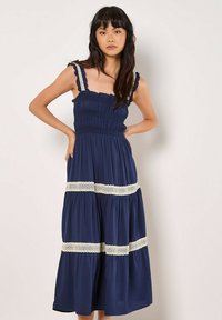 Vestido midi azul marino con cuerpo fruncido, tirantes con volantes y detalles de encaje crema en la cintura y el dobladillo, con un diseño fluido y en capas.