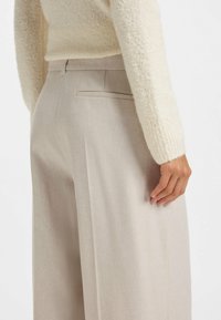 Beige weite Hosen mit glatter Textur, ausgestattet mit einer dezenten Gesäßtasche und einem taillierten Bund, ergänzt durch einen cremefarbenen strukturierten Pullover.